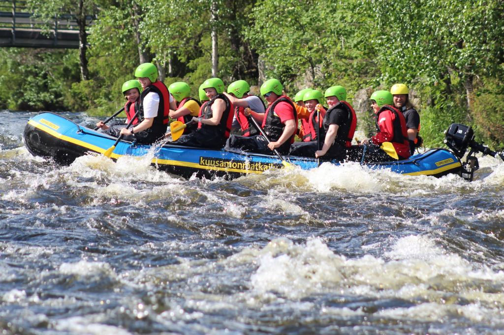 A group of people on an inflatable boat in white water with red safety vests and neon green helmets