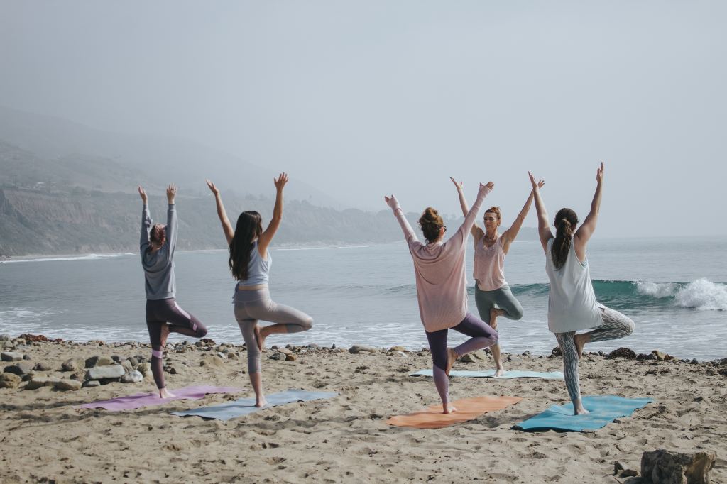Four people take a yoga class on the beach as the waves roll in