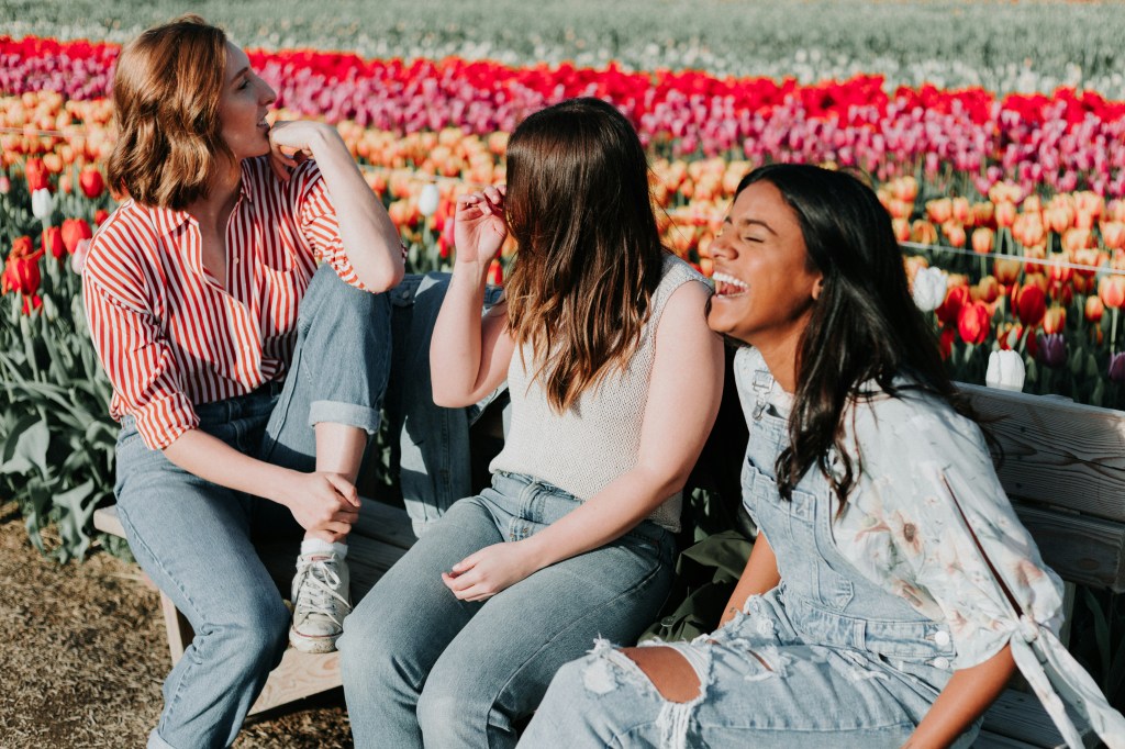 3 women laughing while sitting on bench amidst a tulip farm