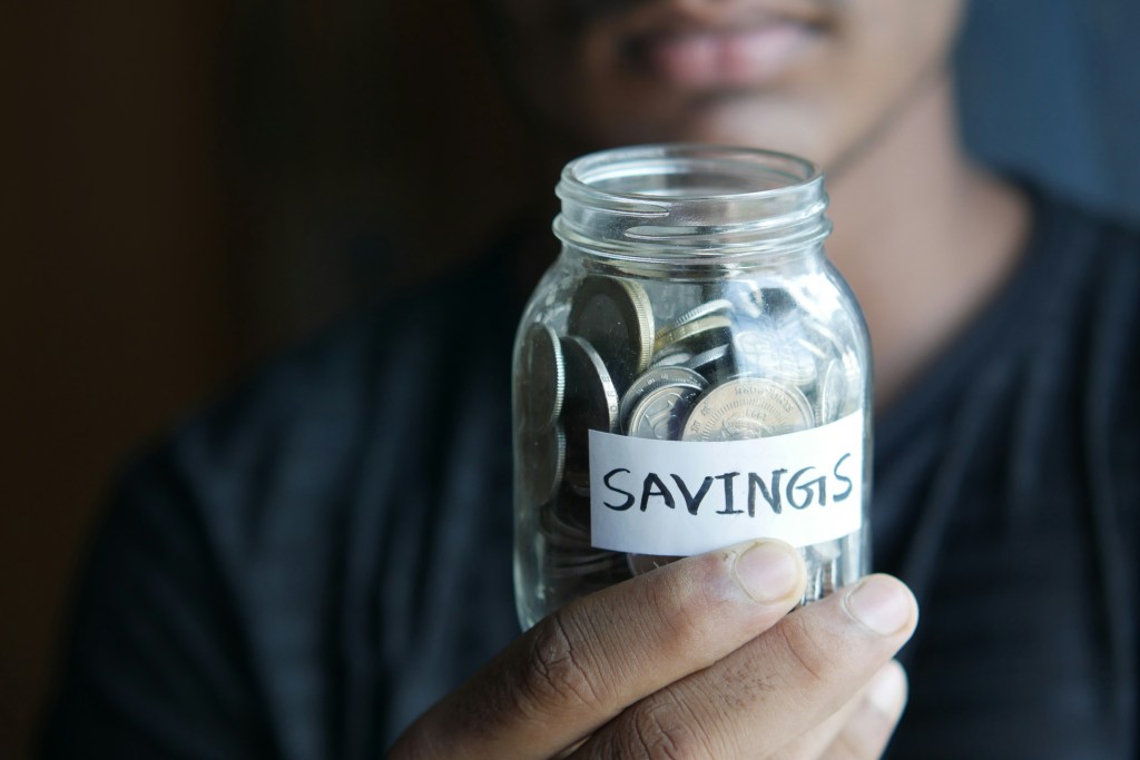 Person holding a jar of coins labeld "savings"