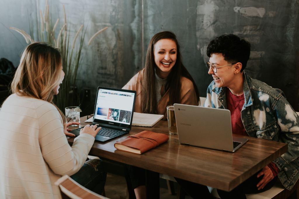 3 friends laughing at a table with their laptops