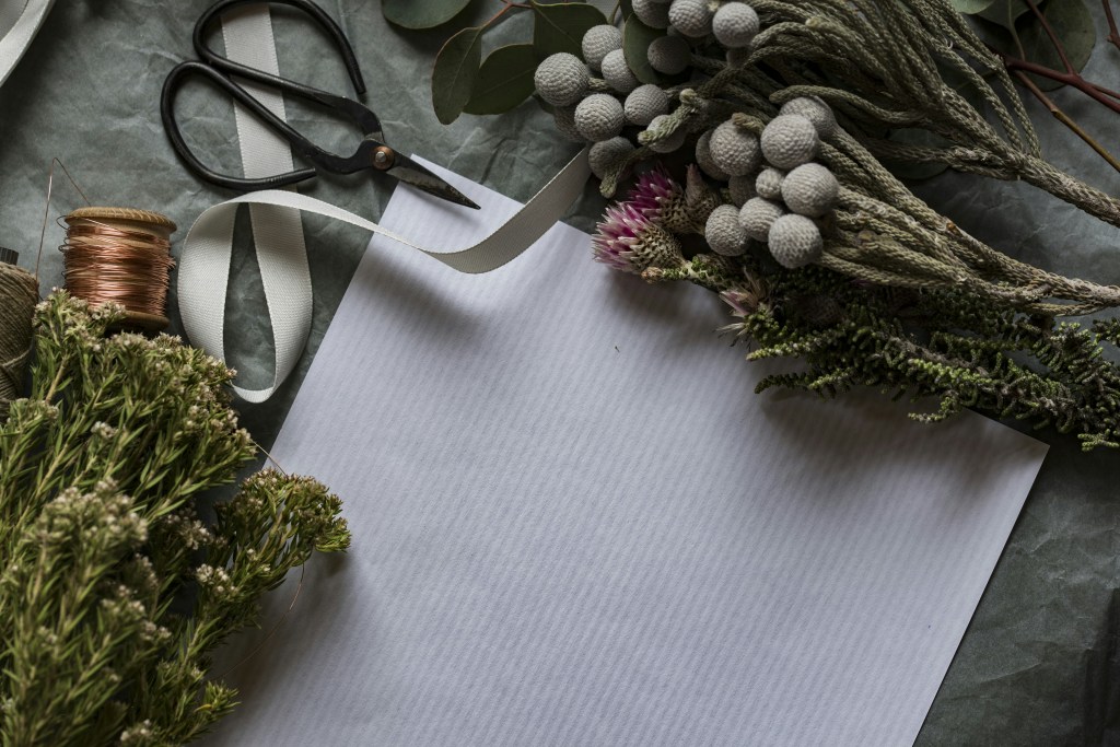 Scissors, ribbons and flowers surrounding a white paper.