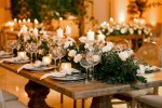 Naked table with lots of small candles on varying height pillars, table settings and greenery with white roses